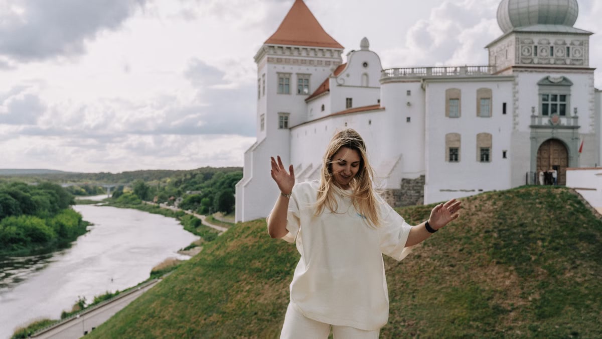 A joyful woman dances in front of a historical castle by a peaceful river.